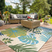 Couristan Covington Indoor/Outdoor Rug - Summer Laelia/Ivory-Fern lies under a patio set, adding a splash of tropical flair to a sunlit wooden deck