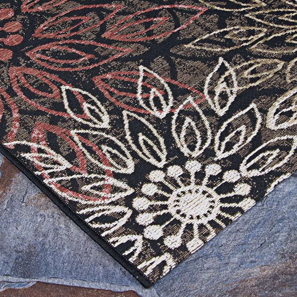 Couristan Dolce Indoor/Outdoor Rug - Amalfi/Multi lies on a stone surface, displaying detailed cream and rust floral patterns on a dark background