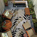 Couristan Dolce Indoor/Outdoor Rug - Aralia/Naturals-Cool Onyx is shown in a cozy patio setup surrounded by wooden outdoor furniture and lush greenery