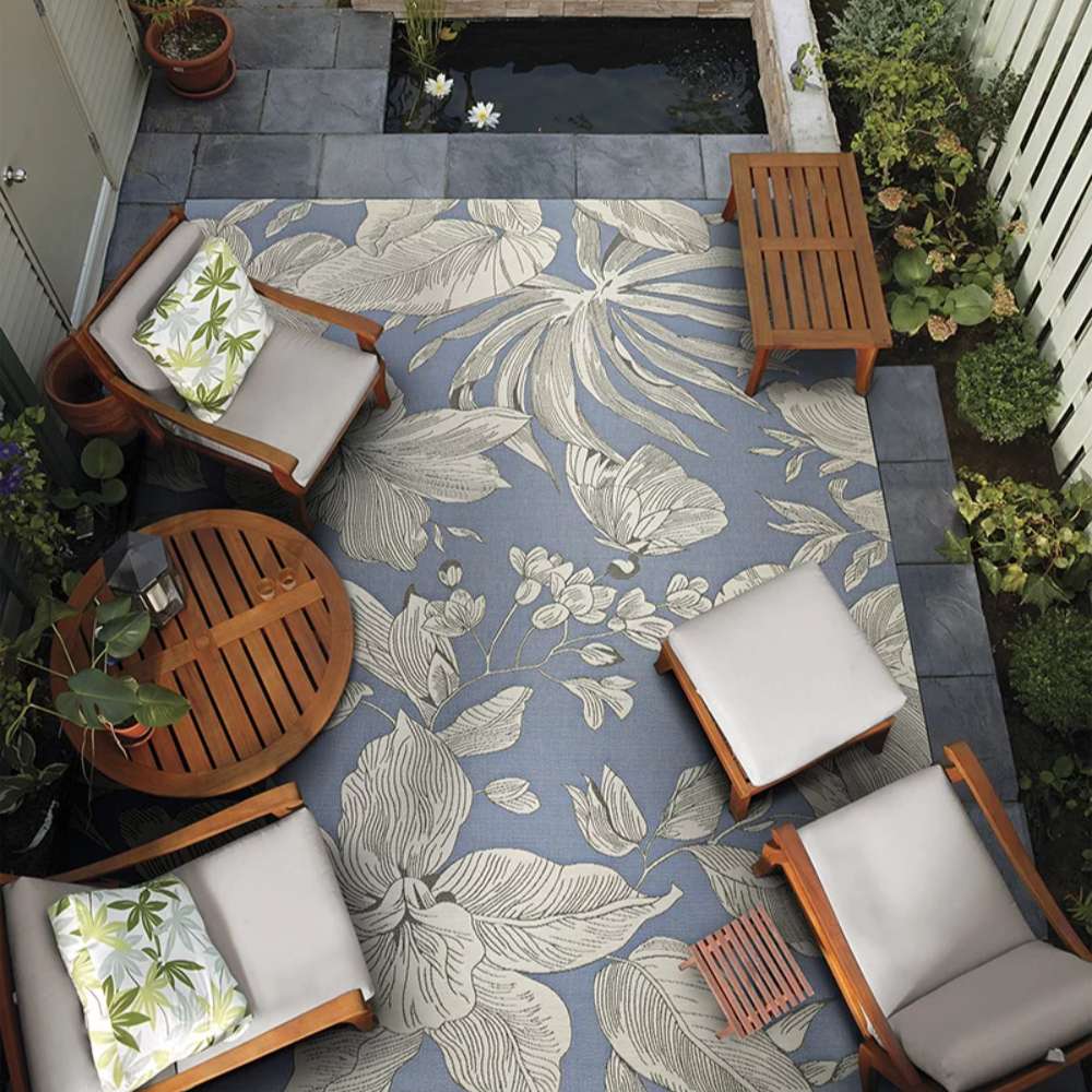 Couristan Dolce Indoor/Outdoor Rug - Flora/Ice is placed on a patio surrounded by wooden chairs and greenery