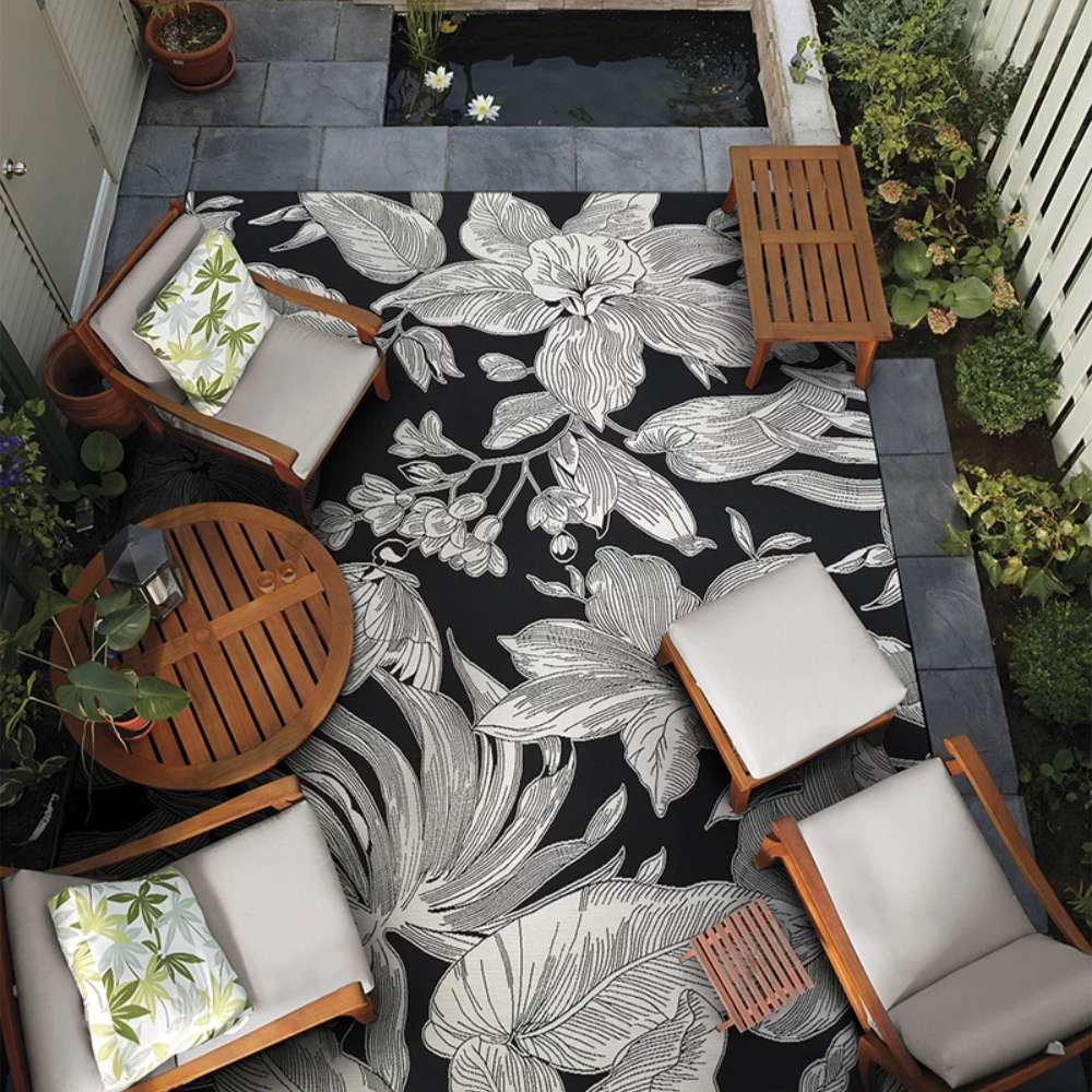 Couristan Dolce Indoor/Outdoor Rug - Flora/Nero is styled in an outdoor patio surrounded by wooden chairs and plants