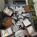 Couristan Dolce Indoor/Outdoor Rug - Flora/Nero is styled in an outdoor patio surrounded by wooden chairs and plants