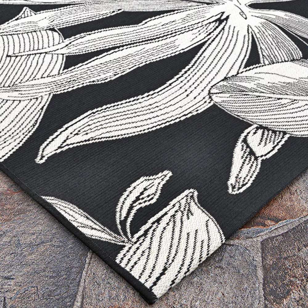Couristan Dolce Indoor/Outdoor Rug - Flora/Nero lies flat on stone tiles featuring bold ivory floral patterns on a deep black background