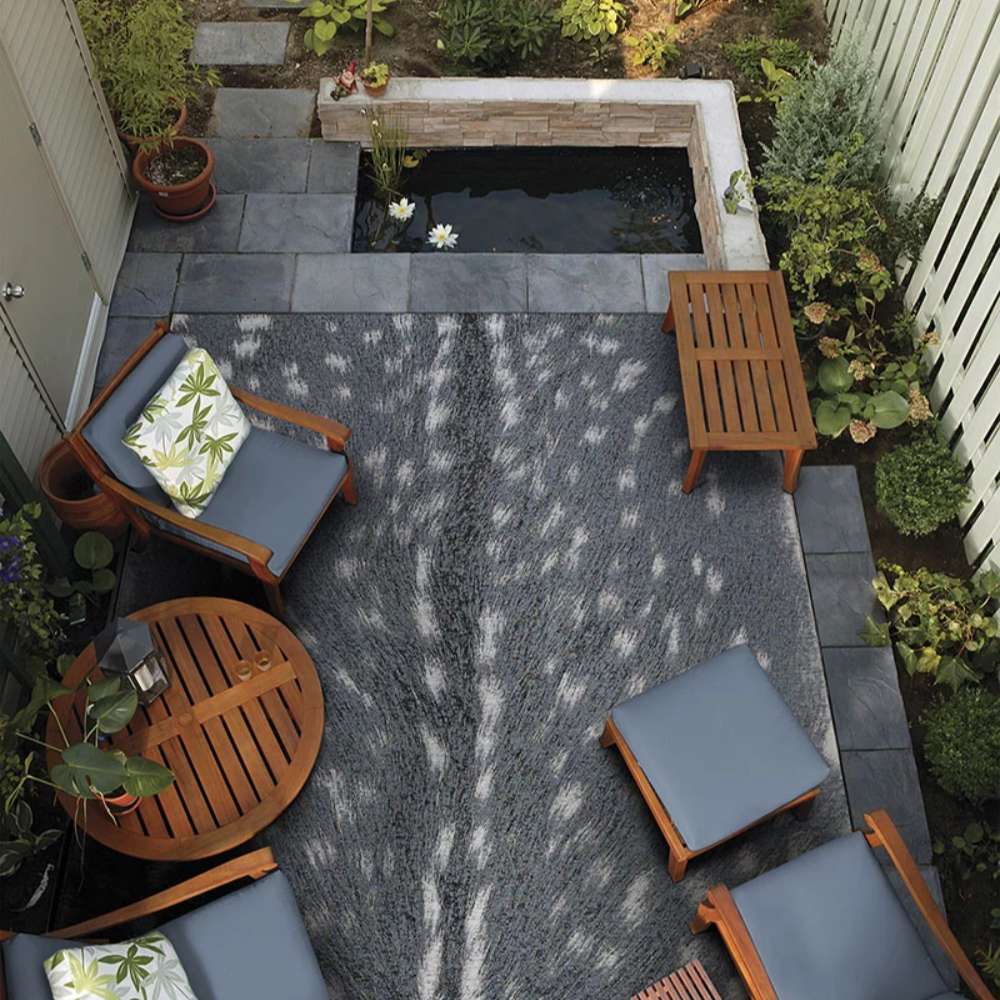 Couristan Dolce Indoor/Outdoor Rug - Hyena/Denim-Silver is beautifully placed in a cozy outdoor patio setting with wooden furniture