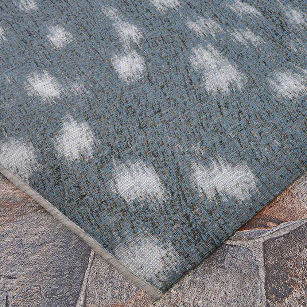 Couristan Dolce Indoor/Outdoor Rug - Hyena/Denim-Silver lies flat on a stone patio with soft ivory patterns on a denim background