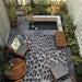 Couristan Dolce Indoor/Outdoor Rug - Lynx/Ivory-Charcoal is laid out on a cozy patio with wood furniture and greenery surrounding a small pond