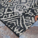 Couristan Dolce Indoor/Outdoor Rug - Mala/Smoke lies flat with sharp, tribal-inspired black and ivory patterns and touches of rust color on a stone patio