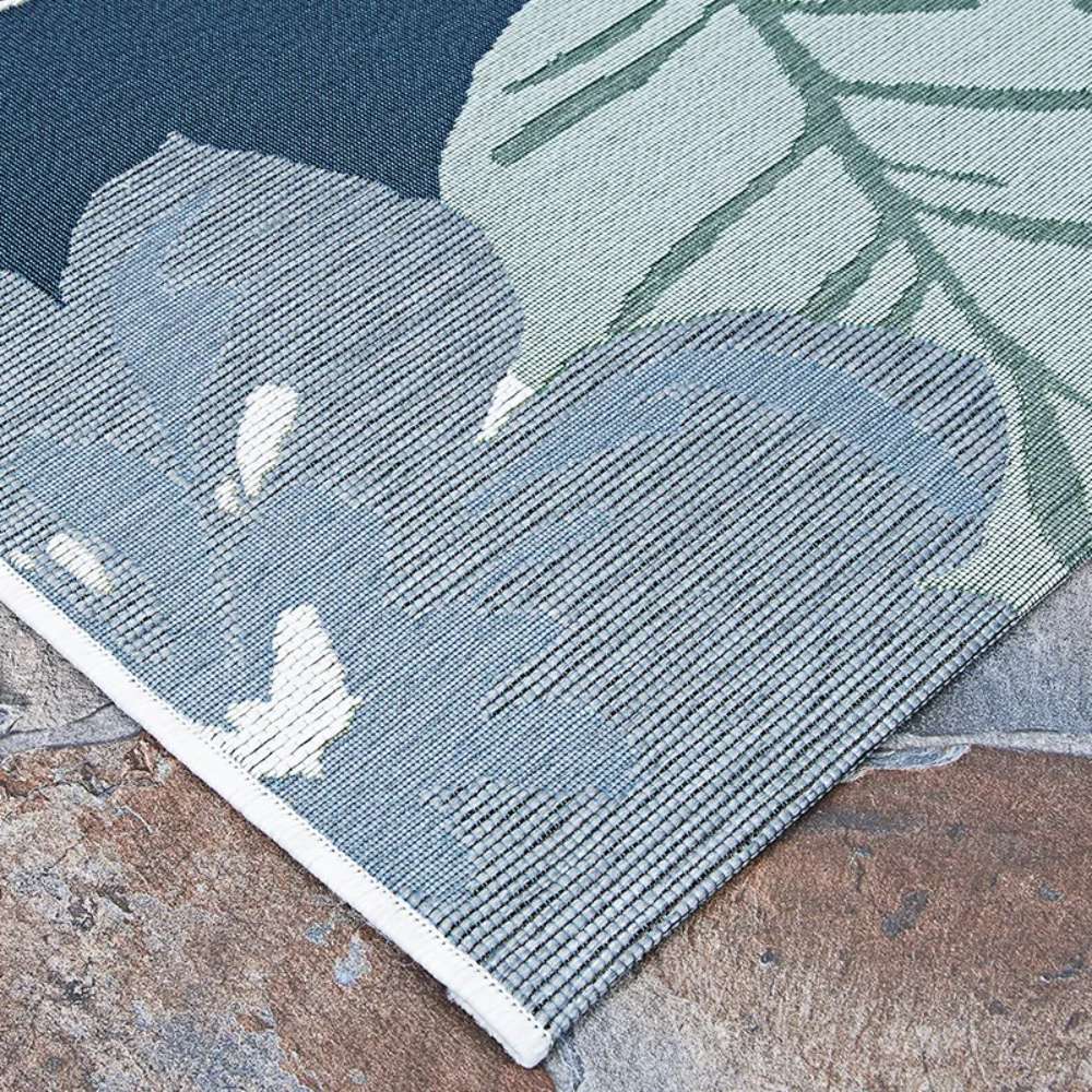 Couristan Dolce Indoor/Outdoor Rug - Novella/Grey displays a leafy floral pattern in shades of blue and green, lying flat on a stone surface