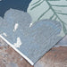 Couristan Dolce Indoor/Outdoor Rug - Novella/Grey displays a leafy floral pattern in shades of blue and green, lying flat on a stone surface