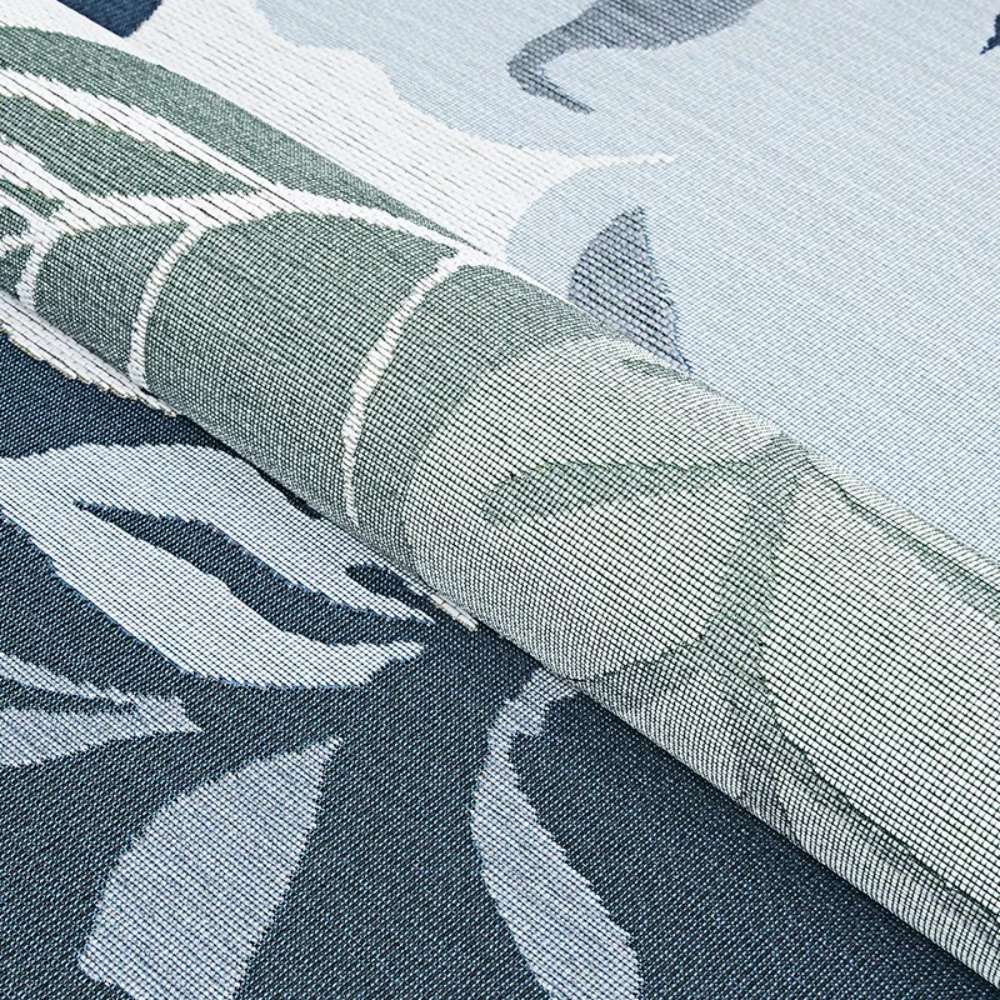 Couristan Dolce Indoor/Outdoor Rug - Novella/Grey is partially rolled, revealing its floral design with green leaves and soft blue tones