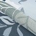 Couristan Dolce Indoor/Outdoor Rug - Novella/Grey is partially rolled, revealing its floral design with green leaves and soft blue tones