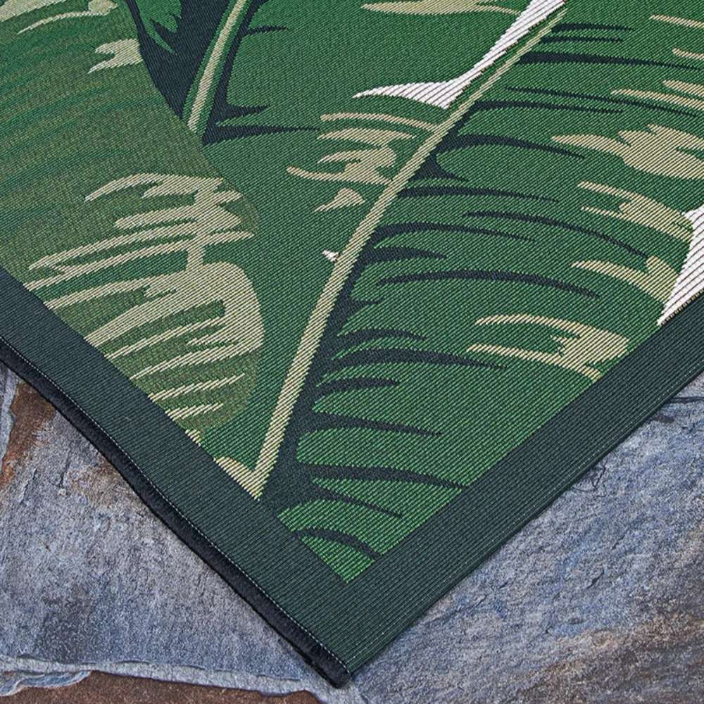 Couristan Dolce Indoor/Outdoor Rug - Palm Lily/Hunter Green-Ivory is shown lying flat on a stone floor with rich green palm leaf patterns and dark green trim
