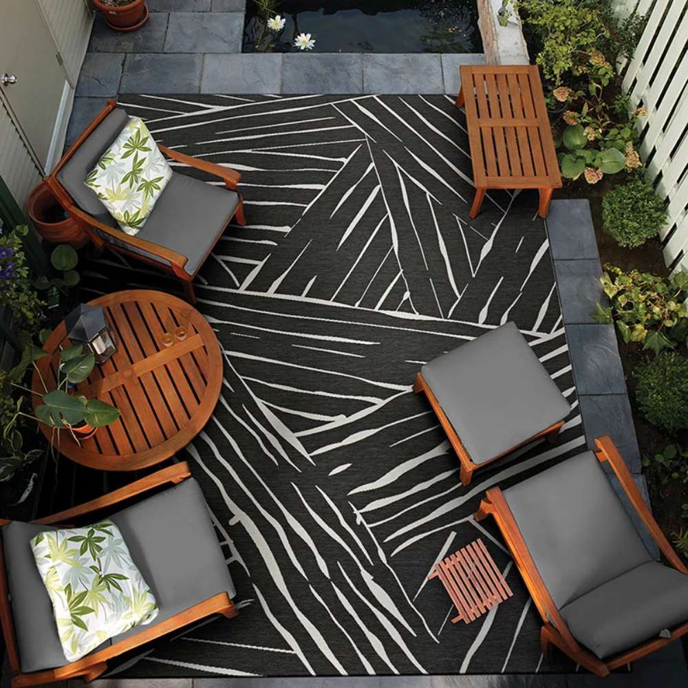 Couristan Dolce Indoor/Outdoor Rug - Parquet/Charcoal is styled in a patio setting with wooden furniture and lush greenery