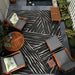 Couristan Dolce Indoor/Outdoor Rug - Parquet/Charcoal is styled in a patio setting with wooden furniture and lush greenery