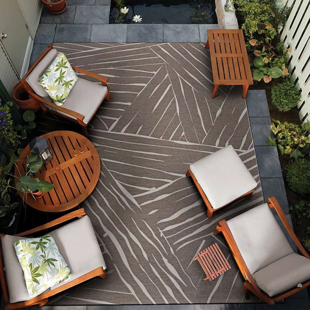 Couristan Dolce Indoor/Outdoor Rug - Parquet/Mocha is displayed on a cozy outdoor patio, surrounded by wooden furniture and lush greenery