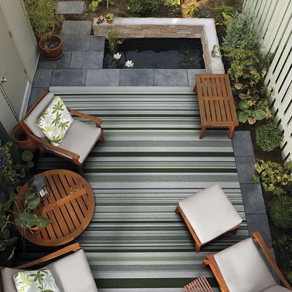 Couristan Dolce Indoor/Outdoor Rug - Striped/Grass is placed in a cozy patio with wooden furniture and a small pond