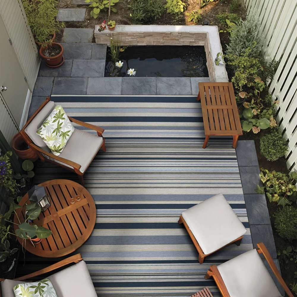 Couristan Dolce Indoor/Outdoor Rug - Striped/Nautical is laid out in a cozy garden patio space surrounded by wooden outdoor furniture