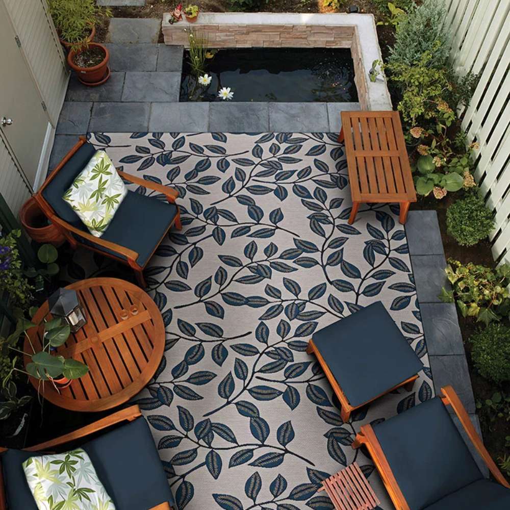 Couristan Dolce Indoor/Outdoor Rug - Summer Ivy/Ivory-Slate Blue is beautifully placed in a cozy outdoor patio surrounded by wooden furniture