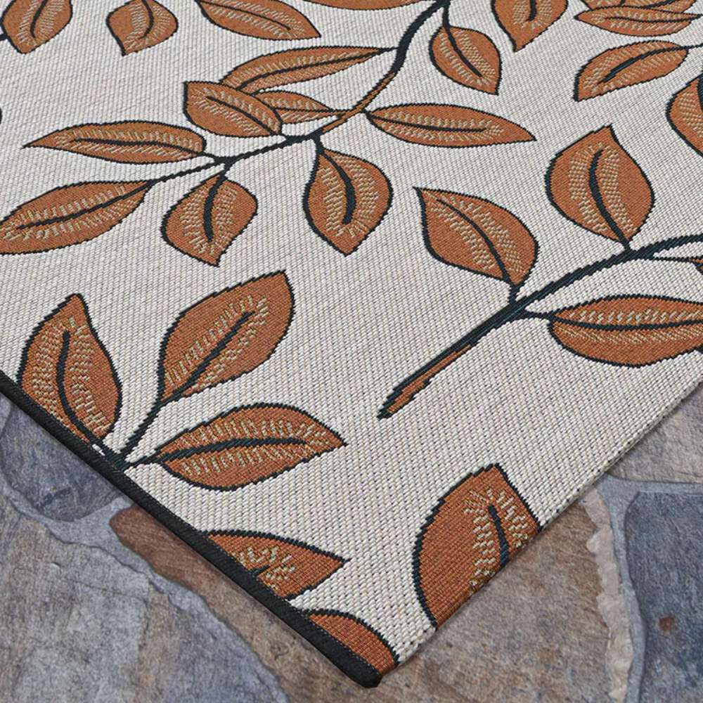 Couristan Dolce Indoor/Outdoor Rug - Summer Ivy/Ivory-Terra-Cotta lies flat on a stone patio displaying a clean edge and leaf pattern