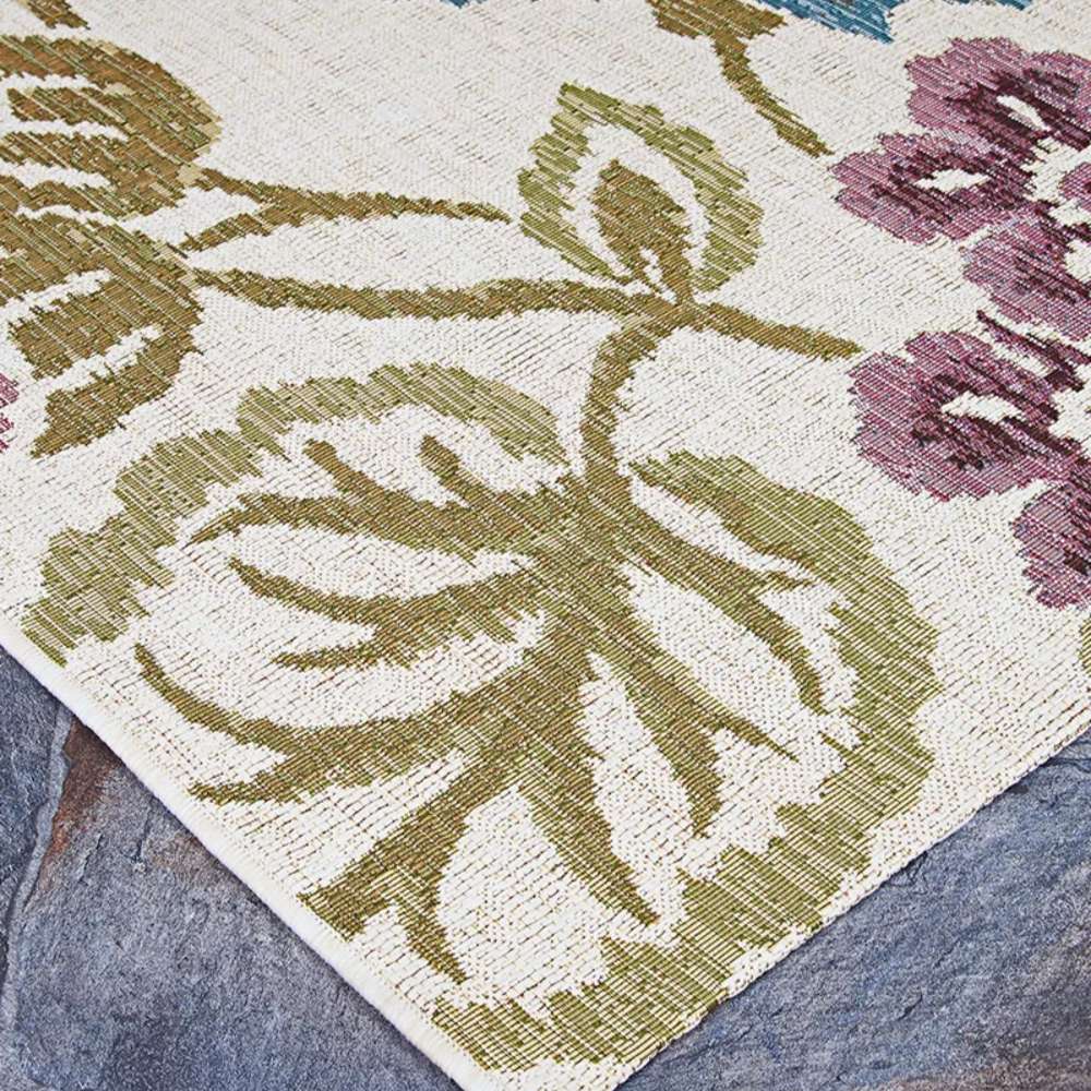 Couristan Dolce Indoor/Outdoor Rug - Tivoli/Ivory-Multi lies flat on a stone surface, displaying leafy green and purple floral patterns on an ivory background