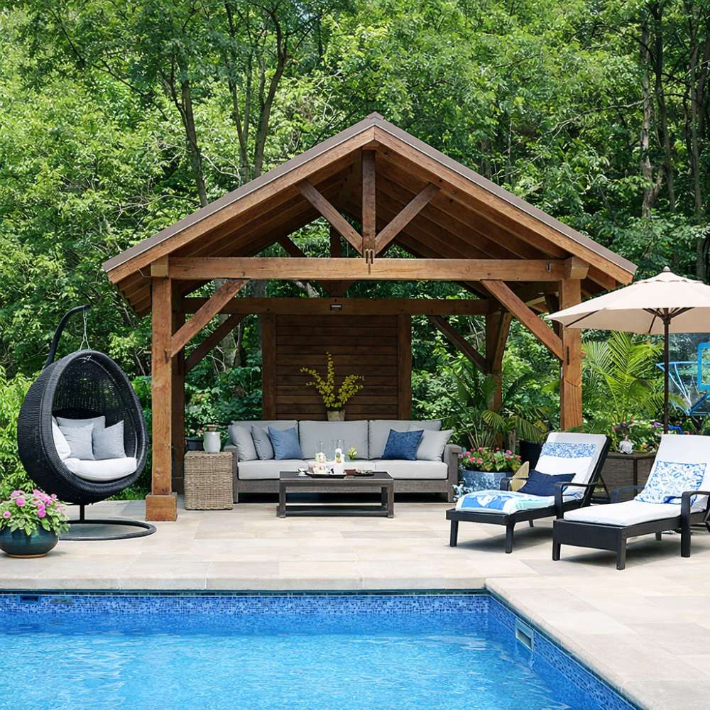 Cozy outdoor seating area sits beneath Brookside Timber Frame Forest Retreat Pavilion, featuring a wooden structure beside a pool surrounded by lush green trees