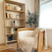 Cozy reading corner features Crate & Barrel Terrazza 38" Natural Solid Oak Wood 5-Shelf Storage Bookshelf filled with books, pottery, plants, and decorative accents
