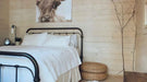 Cozy bedroom with a black metal bed frame, white bedding, and a wall-mounted animal portrait inside the Sawmill Structures Harvest Grand Bungalow 107 Garden Room