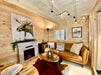 Cozy living space inside the Sawmill Structures Grand Loft 107 Deluxe DD Garden Room includes a brown leather sofa, a fireplace with moose artwork, and warm wooden walls