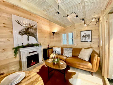 Cozy living space inside the Sawmill Structures Grand Loft 107 Deluxe DD Garden Room includes a brown leather sofa, a fireplace with moose artwork, and warm wooden walls