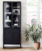 Crate & Barrel Casement 32" Black Storage Cabinet stands beside large windows, with glass shelves displaying books, glassware, and decorative objects above closed lower storage