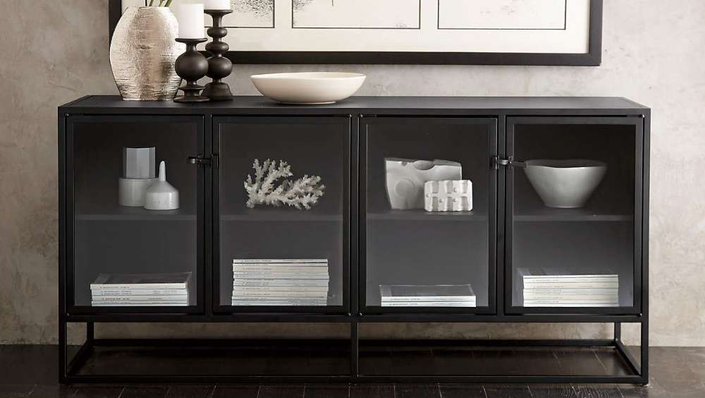 Crate & Barrel Casement 66" Black Credenza displays decorative bowls, books, and accents on two shelves behind smoked glass doors