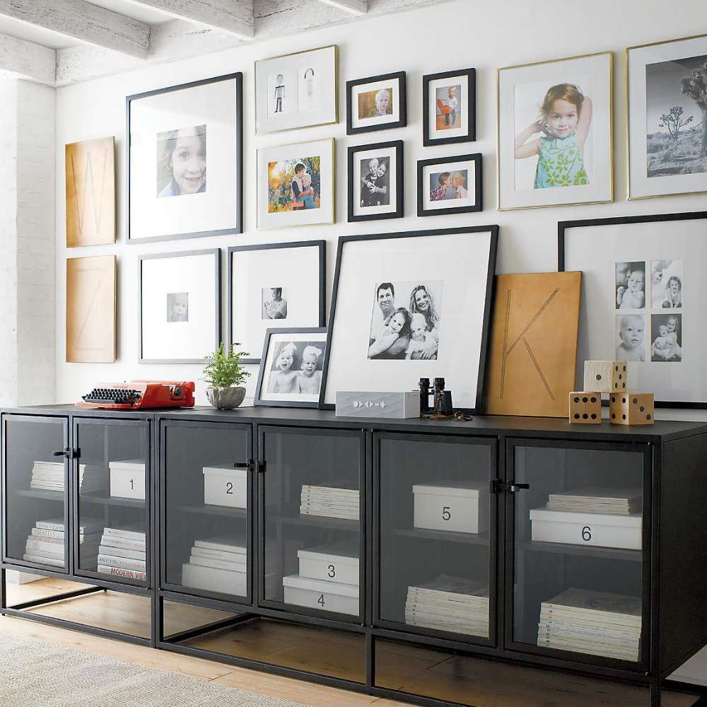 Crate & Barrel Casement 66" Black Credenza stands below a gallery wall, organizing books, storage boxes, and framed photos behind four glass doors