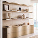 Crate & Barrel Coast 120" Whitewashed Oak Open Storage Bookcase, Set of 3 styled in a bright room with decorative vases, books, and artwork displayed across the wide shelves