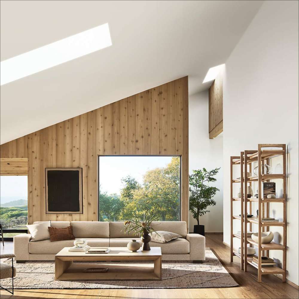 Crate & Barrel Elias Natural Elm Wood Open Bookcase stands against a living room wall, adding open storage and display space beside a modern sofa