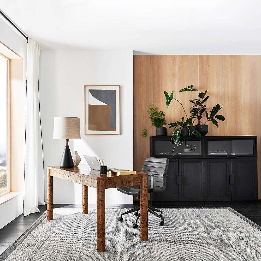 Crate & Barrel Emerson 60" Mappa Burl Desk styled in a modern home office with a task chair, table lamp, laptop, and black storage cabinets