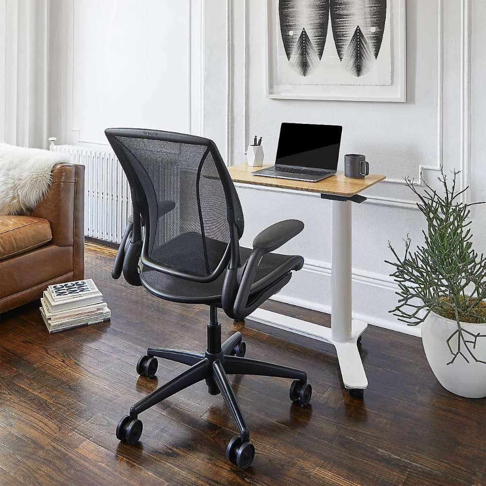 Crate & Barrel Humanscale® World LM Seat Task Office Chair is positioned beside a height-adjustable desk with a laptop in a stylish living room workspace