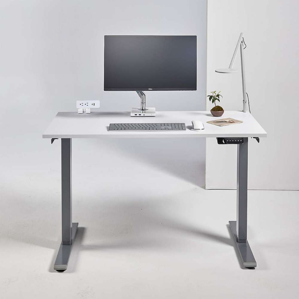 Crate & Barrel Humanscale® eFloat Go 2.0 60" White Adjustable Standing Charging Desk styled with a monitor, keyboard, mouse, desk lamp, and small plant in a modern workspace