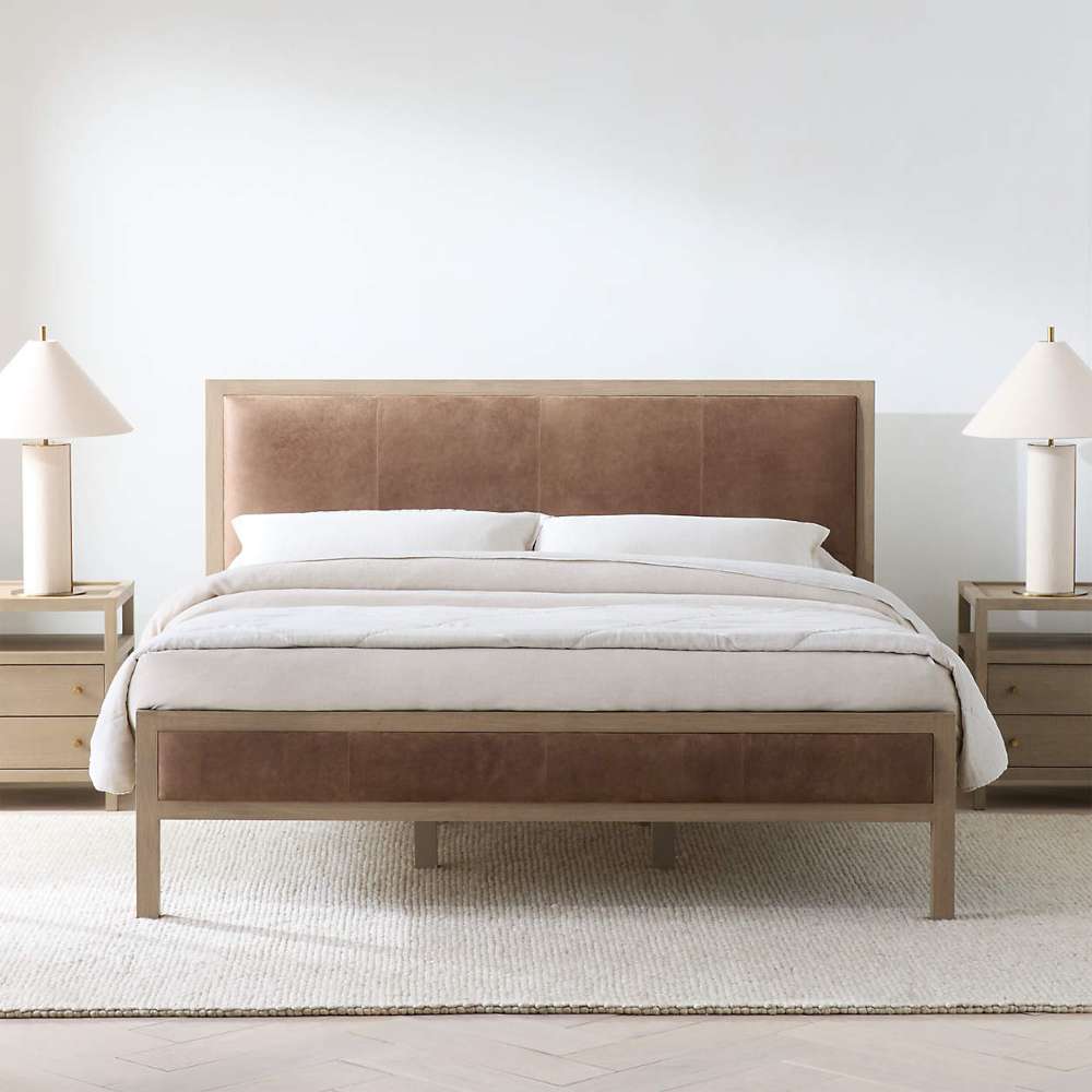 Crate & Barrel Keane Weathered Natural Wood and Leather Queen Bed is shown in a bright bedroom with matching nightstands, white bedding, and warm leather panels