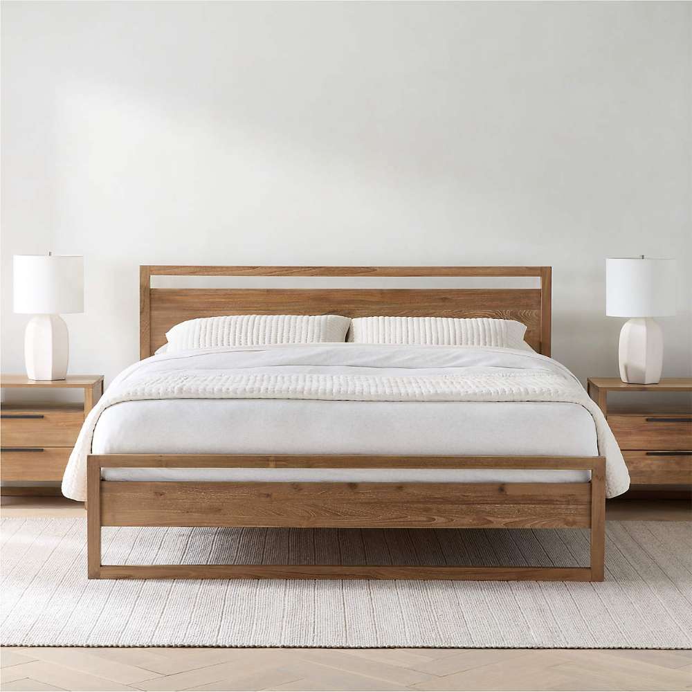 Crate & Barrel Linea Natural Teak Wood Bed centered in a simple bedroom with white bedding, matching nightstands, lamps, and a neutral rug