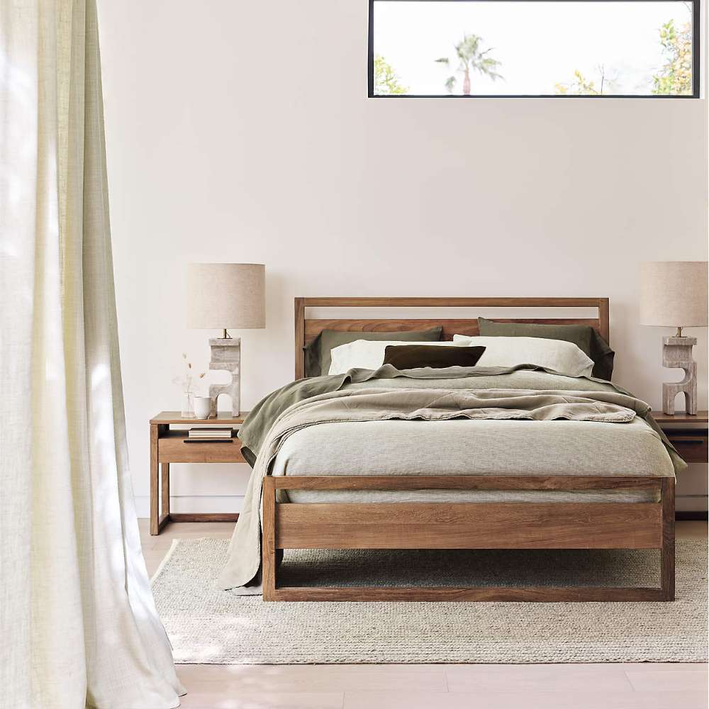 Crate & Barrel Linea Natural Teak Wood Bed in a calm bedroom with green bedding, matching wood nightstands, table lamps, and soft curtains