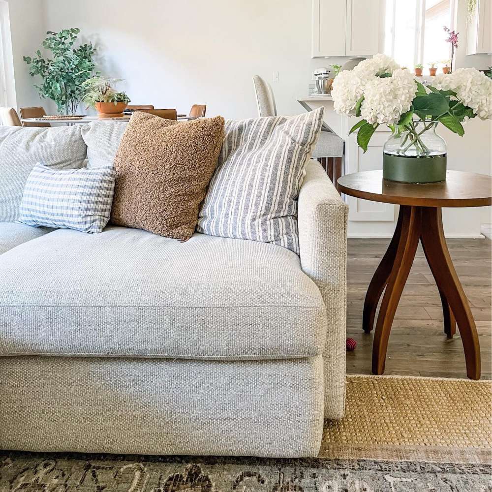 Crate & Barrel Lounge Sofa displayed in a bright living room with layered accent pillows beside a round wood side table with fresh flowers