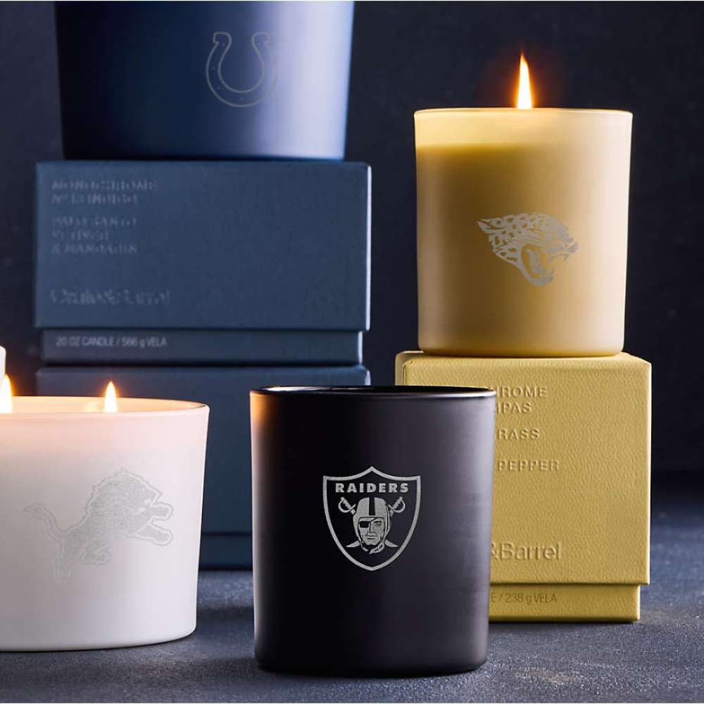 Crate & Barrel Monochrome Scented Candle collection displayed in black, white, and gold vessels with NFL team logos and glowing flames
