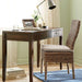 Crate & Barrel Morris 48" Chocolate Brown Writing Desk styled in a bright room with a woven chair, desk lamp, framed photo, and decorative accents