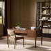 Crate & Barrel Morris 60" Chocolate Brown Writing Desk styled in a warm office with a cushioned chair, bookshelves, and decorative accents