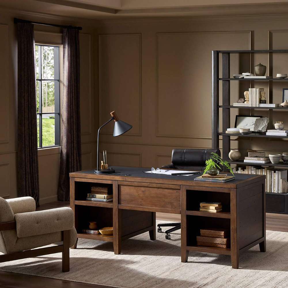 Crate & Barrel Morris 72" Chocolate Brown Writing Desk styled in a home office with open shelves, a desk lamp, books, and a rolling chair