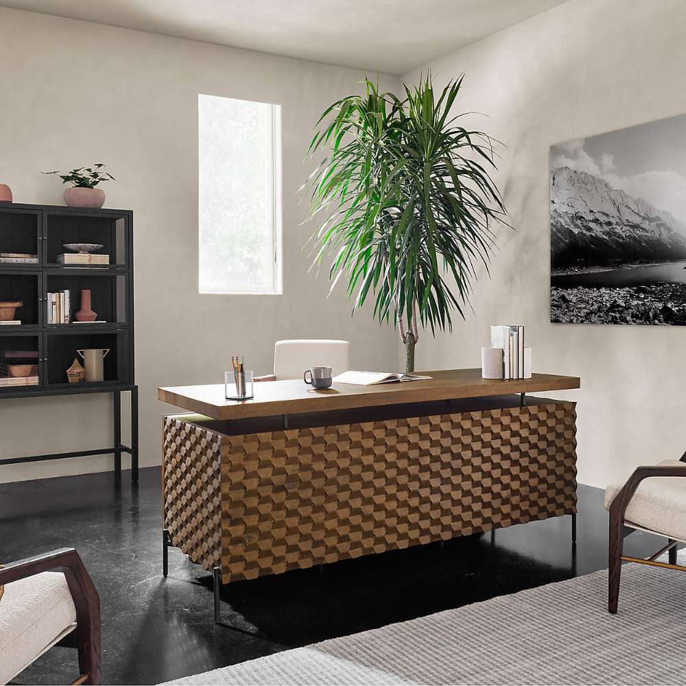 Crate & Barrel Raffael Carved Wood Executive Desk placed in a modern office with a large plant and contemporary decor