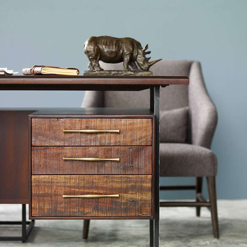 Crate & Barrel Sedgwick Solid Acacia Wood Desk with Storage features three wood drawers with brass handles beneath the desktop and a decorative rhino sculpture on top
