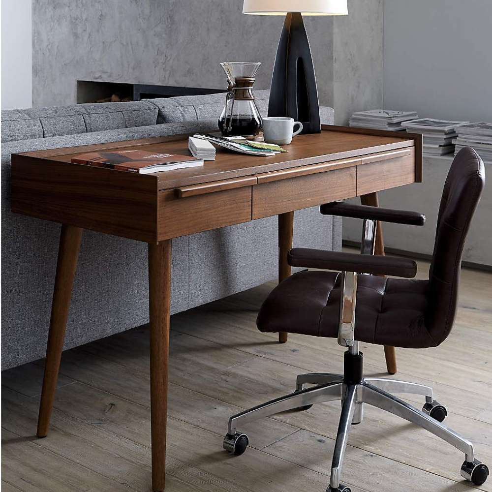 Crate & Barrel Tate 48" Walnut Desk with Outlet styled in a living room workspace beside a sofa, with decorative items displayed on its desktop