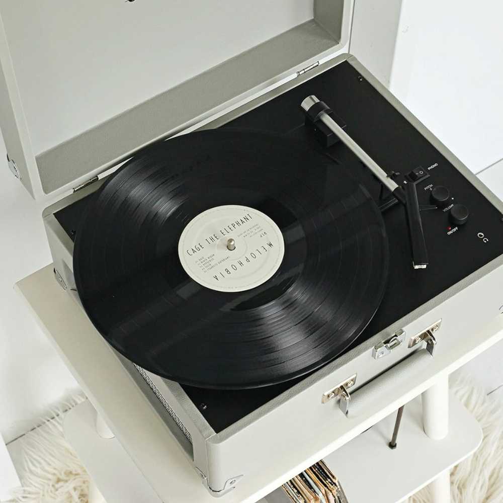 Crosley Anthology Portable Turntable - Gray playing a black vinyl record with a simple, retro design placed on a white shelf