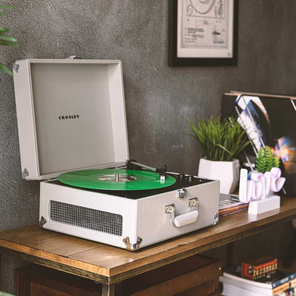 Crosley Anthology Portable Turntable - Gray playing a green vinyl record on a wooden table with plants, decor, and records in the background